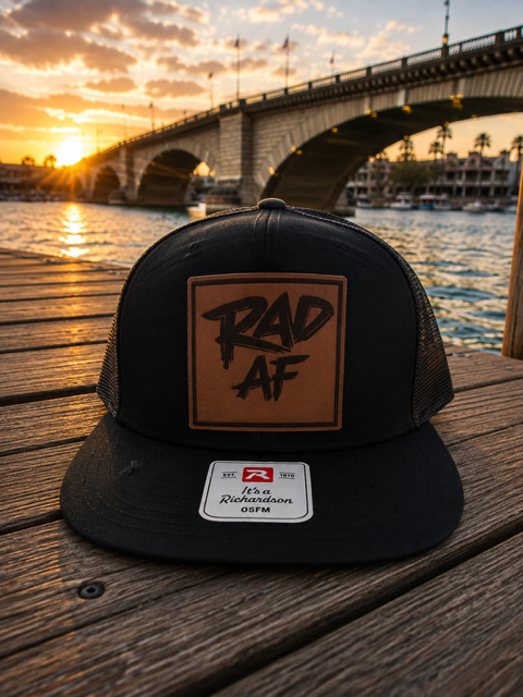 Black trucker hat with RAD AF leather patch on a dock at sunset